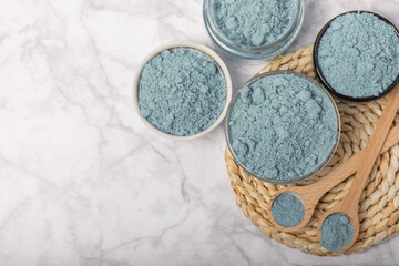 Blue spirulina powder in bowls and spoon on white marble background. Natural vegan superfood. food supplement. place for text. Copy space.