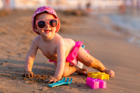 Sweet baby girl playing on sand at the beach with plastic toys.