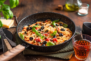 Obraz na płótnie Canvas Spaghetti pasta with tomatoes sauce, black olives, capers, parmesan and fresh basil. Dark wooden table background