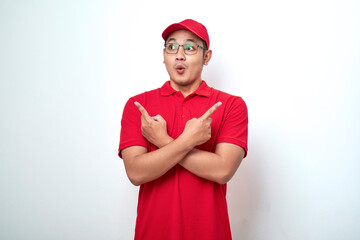 Confused asian courier man in red uniform, cap and t-shirt, pointing sideways look interested left