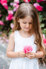 Cute smiling child girl 5-6 year old holding pink rose flower over nature background outdoor. Childhood. Springtime.