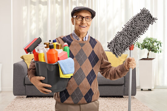 Elderly man holding a bucket with cleaning supplies and a floor mop in a living room - Powered by Adobe