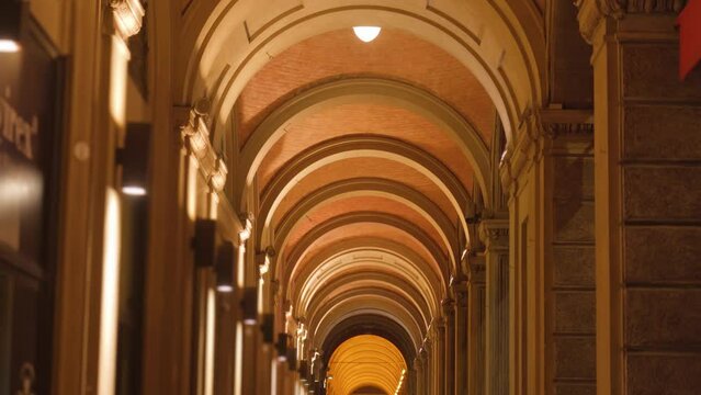 Long ancient building medieval portico with high semi-circular ceiling and columns illuminated with white light in evening in Bologna