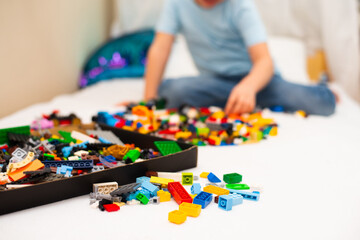 Color blocks of a small constructor on a children's bed in the background a boy in a blue T-shirt sits