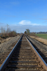 Fototapeta premium Steel railway lines converge to vanishing point on blue sky day with no people