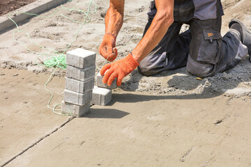 A worker on a sandy surface sets a level with a stretched nylon thread for laying paving slabs on a...
