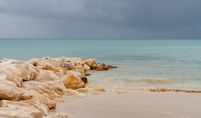 Antigua beach and rock jetty with gentle waves and storm clouds on calm sea