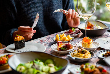 woman hand eating food in restaurant. wine, cheese, meat, vegetables and other appetizers on table