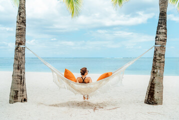 Young woman relaxing in wicker hammock on the sandy beach on Mauritius coast and enjoying wide...