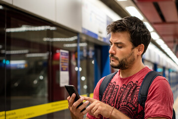 Fototapeta na wymiar Hombre en estación de subte verificando su recorrido en tren en una aplicación de su celular 
