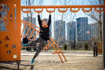 Cute boy is climbing on the playground in the schoolyard. He has a very happy face and enjoy this adventure sports alone outdoor. Warm sunny day
