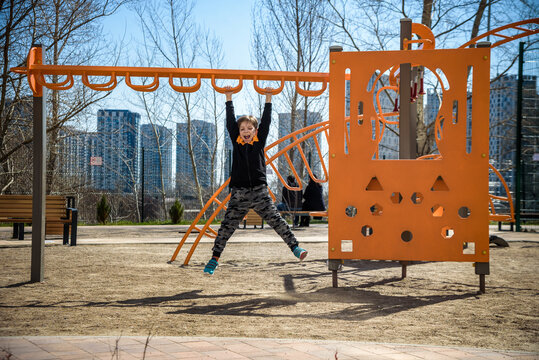 Cute boy is climbing on the playground in the schoolyard. He has a very happy face and enjoy this adventure sports alone outdoor. Warm sunny day