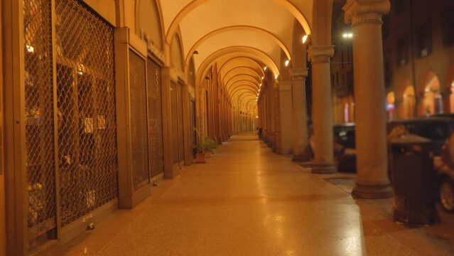 Dim and dark historical building medieval portico passage with marble columns at poor night lighting against cars in narrow street in Bologna
