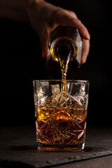 The bartender pours whiskey or rum into a glass, close-up