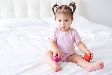 Fototapeta premium funny baby girl in pink bodysuit playing with children wooden cubes toys on bed