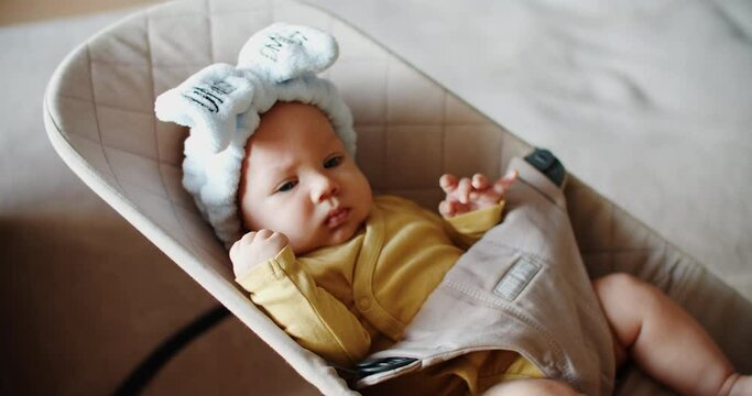 A little baby girl with a big bow on her head lies on a swing or deck chair and rides. child portrait. High quality 4k footage