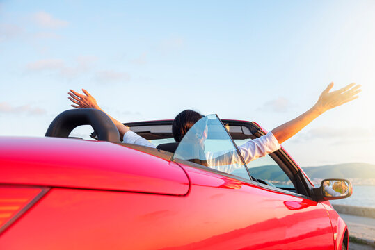 Woman in red car with open roof at background of sea water. Travel, freedom and holidays concept.