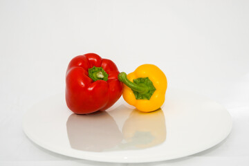Two Capsicum on white plate and background, red and yellow.