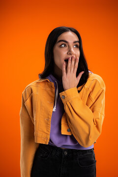 Shocked Young Woman Covering Mouth With Hand Isolated On Orange.