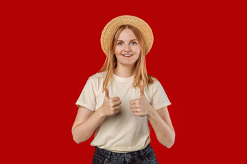 Saying yes. Smiling positive woman with blond hair and denim clothes, showing thumb up to like and approve, praise good thing, recommending product, red background. 