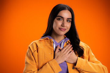 happy young woman touching chest isolated on orange.