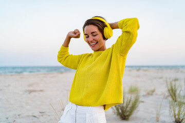 happy smiling woman listening to music in colorful yellow headphones on beach in summer