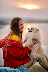 Lady with cute white spitz dog sit on top of mountain enjoying time during travel, adorable pretty...