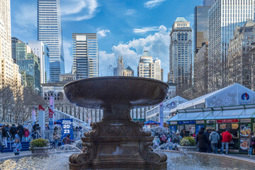 Bryant Park, New York City, daytime, Christmas, large fountain in foreground, crowds of people and...