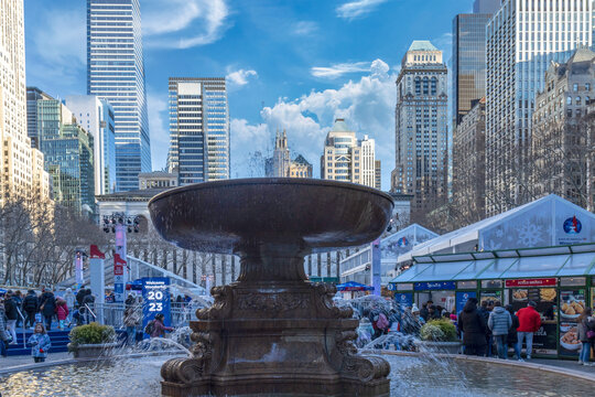 Bryant Park, New York City, daytime, Christmas, large fountain in foreground, crowds of people and city skyline, sunny with clouds
