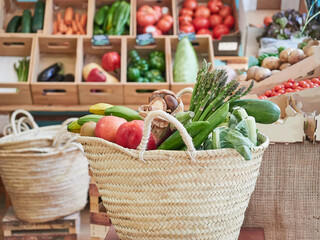 Wicker basket full of vegetables and fruits in a small local organic food store. In the background, shelves with other products in wooden boxes. Healthy and sustainable lifestyle concept.