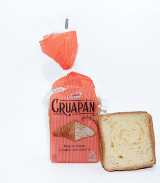 Paquete cerrado de cruap&aacute;n de color naranja y con una foto de un cruas&aacute;n fuera, sobre un fondo blanco con una rebanada cortada apoyada sobre el