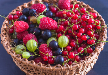 Close up for wicker basket with fresh ripe berries: raspberries, gooseberries, blackberries