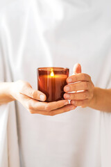 Woman in white clothing holding burning candle close-up in hands. Mock up for candle shop. Stories format advertising aromatherapy or candle handmade masterclass businesses. Church poster. 