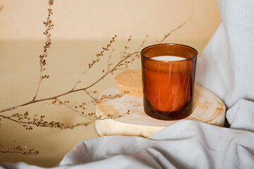 Meditation space with scanted candle. Burning candle on wooden coaster. Warm interior aesthetic composition with dry boho branch and grey fabric. Home comfort, spa, relax and wellness concept, banner