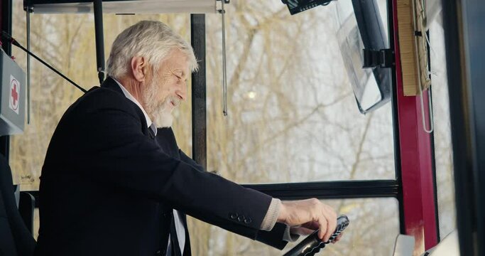 Side view of bus driver putting hands on helm. Old man with grey hair sitting, looking forward, wearing suit and tie, exhausted. Concept of public transport and urban settings.