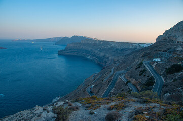 A winding road leading down the cliffs of Santorini at Sunrise with a beautiful Bay below