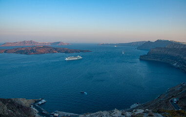 A beautiful landscape of Santorini Islands at sunrise with cruise ships and boats going by in the bay and a harbor and Road below