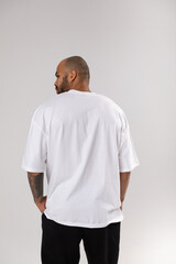 Back view of a bald african american guy with a beard in a white blank t-shirt. Mock-up.