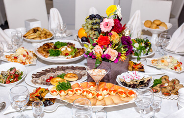 Table setting in a restaurant. Table decorated with flowers and beautiful appetizers salads on a white tablecloth. Holiday dinner.