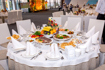 Table setting in a restaurant. Table decorated with flowers and beautiful appetizers salads on a white tablecloth. Holiday dinner.