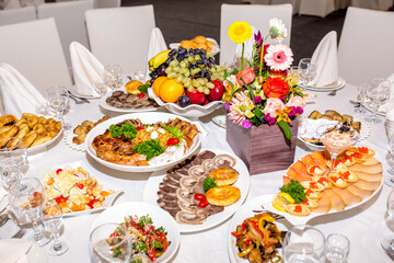 Table setting in a restaurant. Table decorated with flowers and beautiful appetizers salads on a white tablecloth. Holiday dinner.