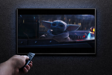 Naklejka premium TV screen playing Mandalorian trailer or movie. Man turns on TV with remote control. Moscow, Russia - January 18, 2023.