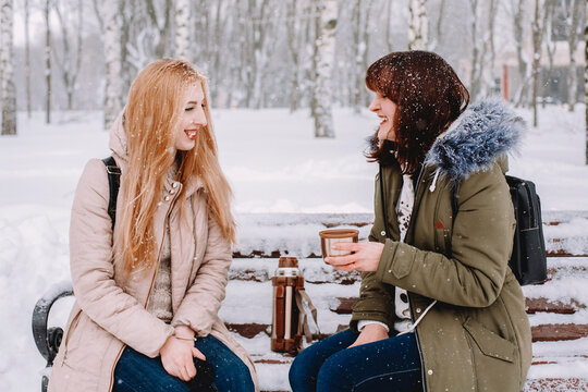 Happy lesbian couple talking while sitting on bench in park during snowfall