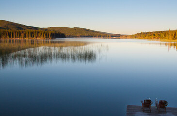 Two chairs on a dock look out on a peaceful lake in British Columbia, Canada.