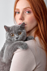 Lovely young woman holding british gray cat isolated on white studio background, good-looking redhead lady in casual wear posing at camera with cat, portrait. pets animals and people concept