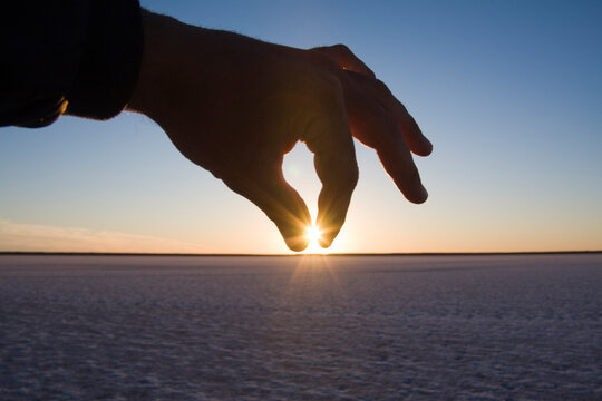 A hand pinches the setting sun over the salt flats on Laguna San Ignacio, Baja California, Mexico.