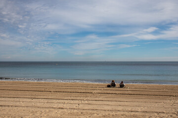 Couple sitting on a beach facing the sea in winter, Spain