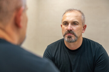 Middle-aged handsome man looking in mirror in bathroom after shaving