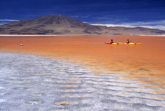 Two kayakers paddle the bright red waters in Bolivia's Laguna Colorada.