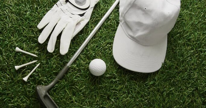 Close up of golf club, ball, glove and peaked cap on grass, copy space, slow motion